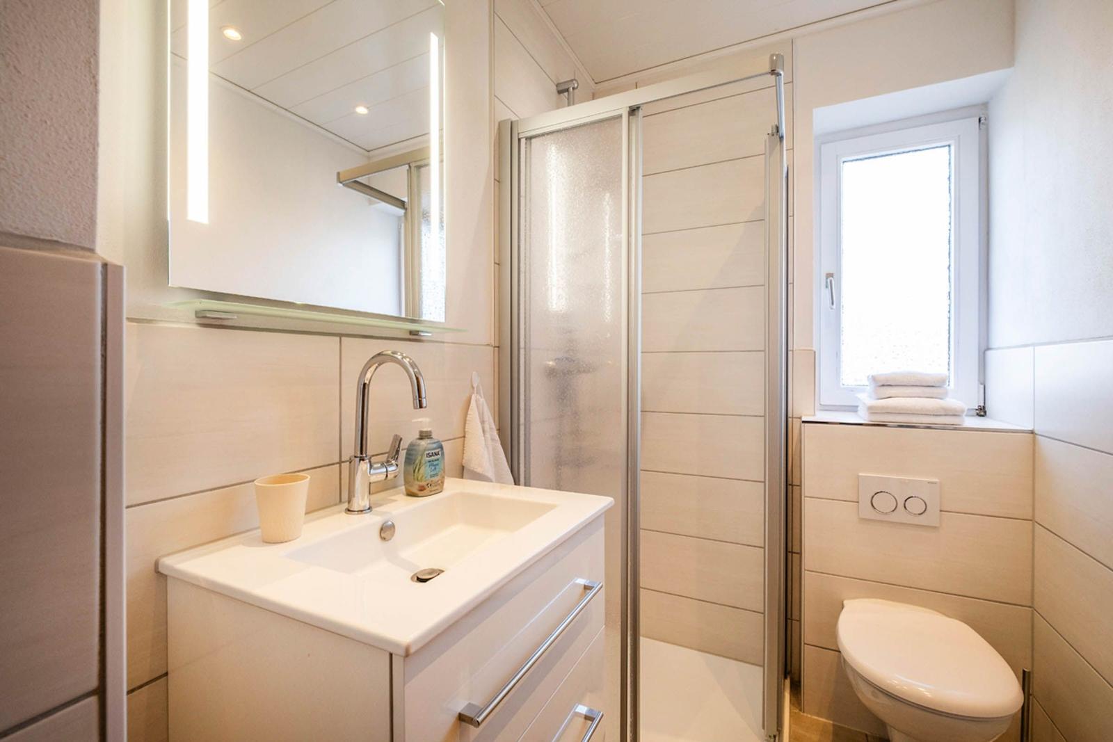 Badezimmer mit Dusche, Waschbecken und Toilette. Fenster mit Handtüchern.