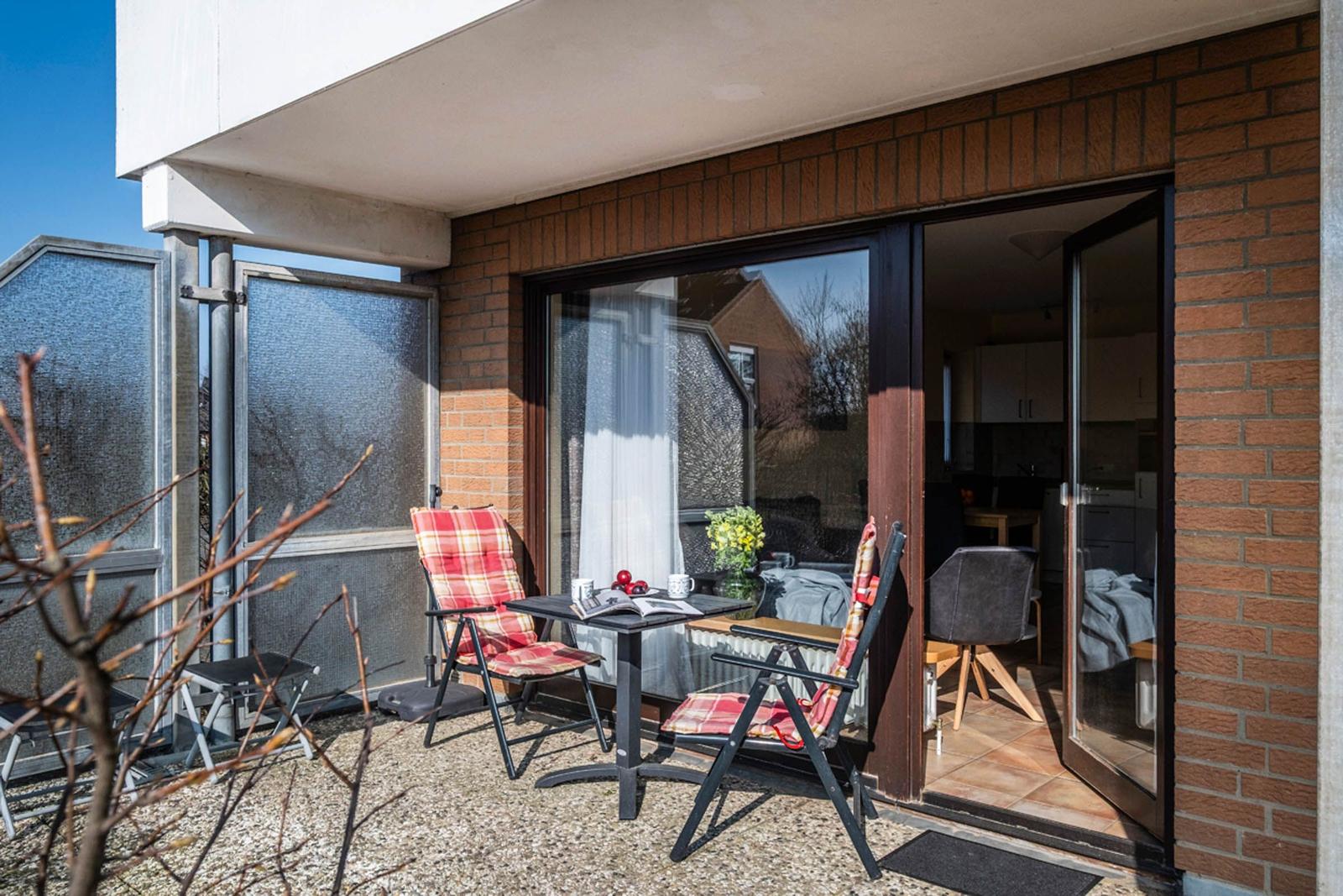 Terrasse mit zwei Stühlen und Tisch, Zugang zum Innenraum über Glastür.