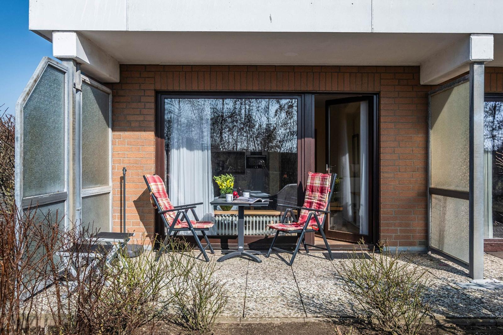 Terrasse mit zwei Stühlen und Tisch vor einem Haus mit Glasfront.