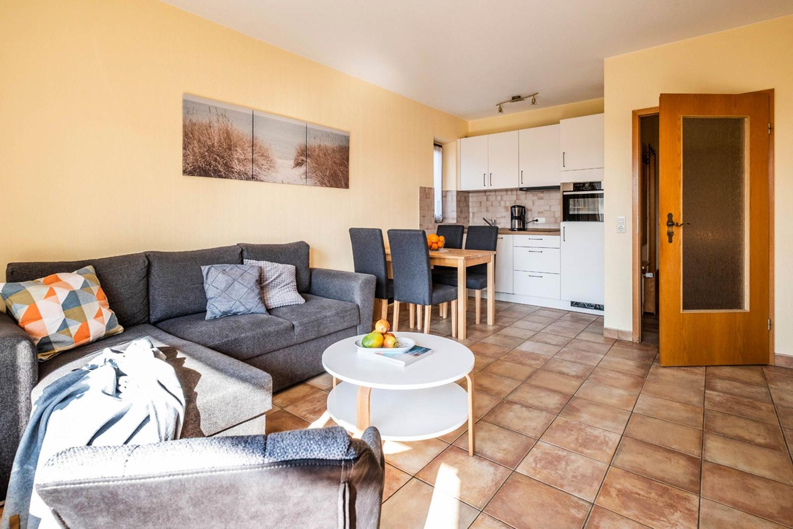Wohn- und Essbereich mit Sofa, Esstisch und Küche im Hintergrund.