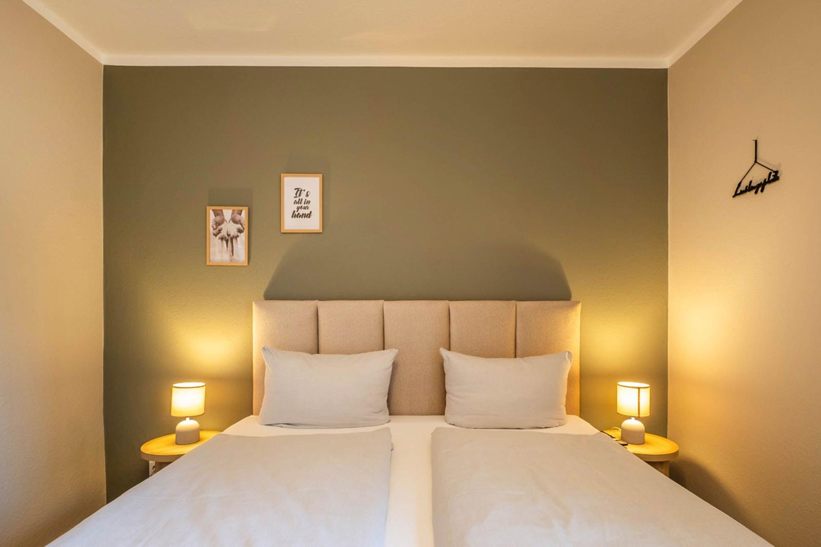 Schlafzimmer mit Bett, Nachttischen und Wandbildern.
