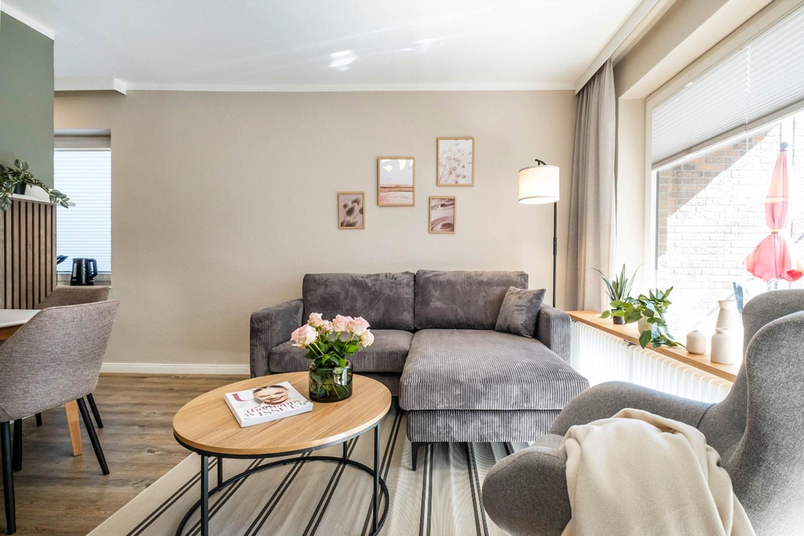 Wohnzimmer mit grauem Sofa, runden Tisch und Fenster mit Blick nach draußen.