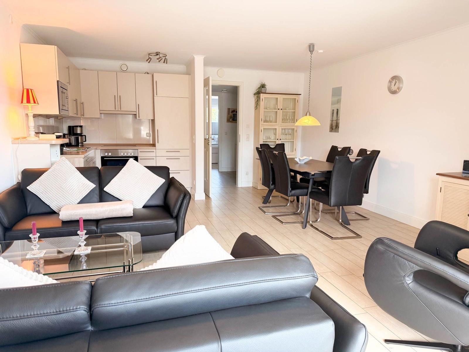 Living and dining area with black leather furniture and modern kitchen.