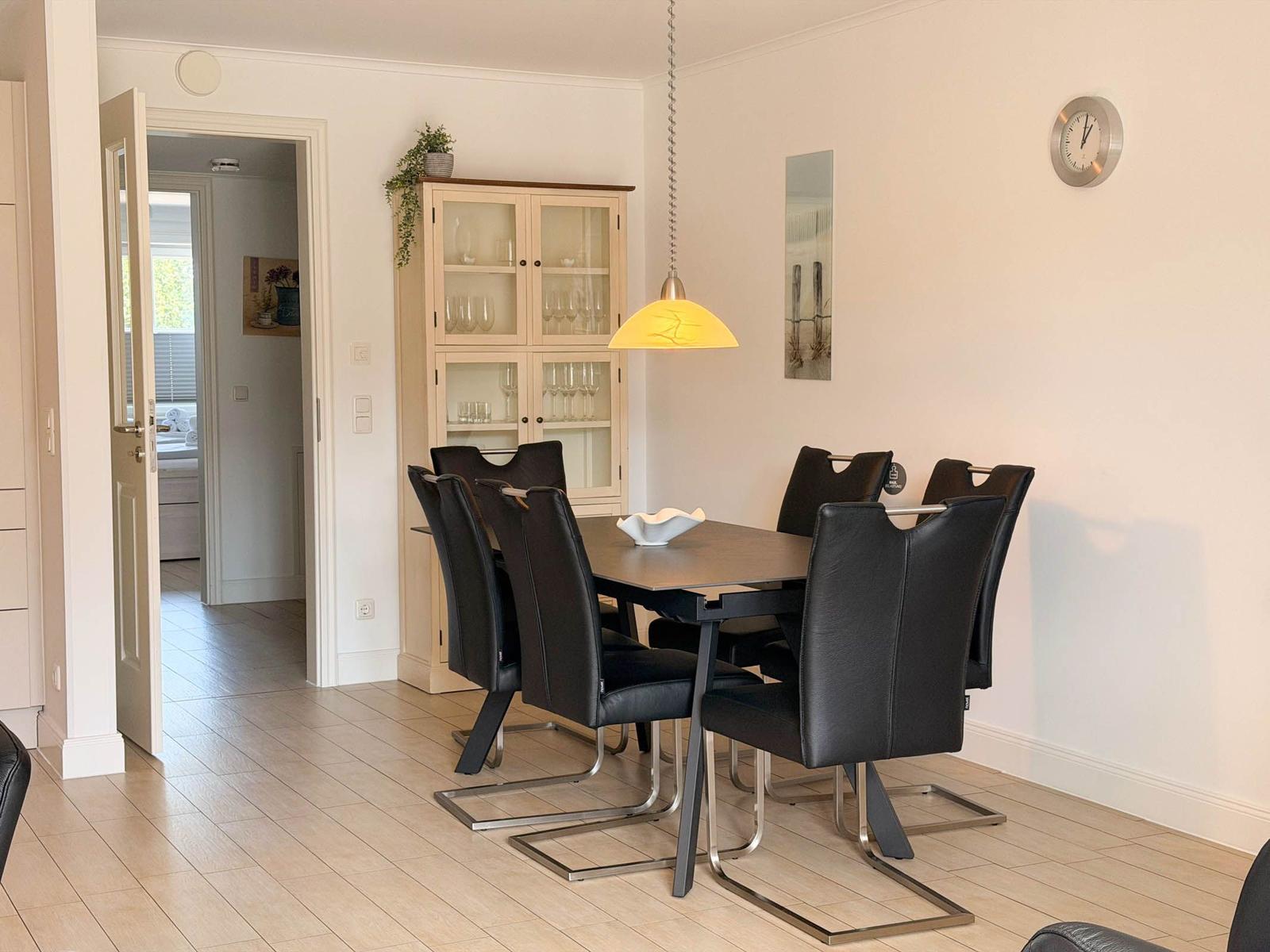 Dining room with table, six chairs, and glass cabinet. Pendant lamp and wall clock visible.