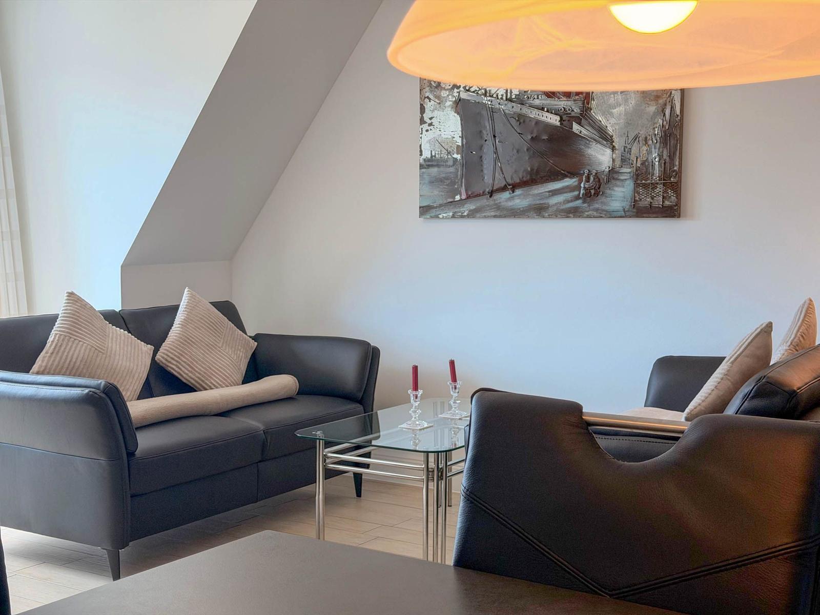 Living room with sofa, armchair, and glass table under a ceiling lamp.