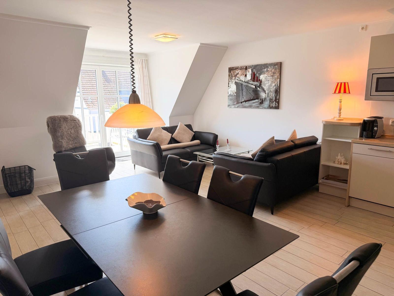 Living and dining area with sofa, dining table, and kitchenette. Window to outdoor terrace.
