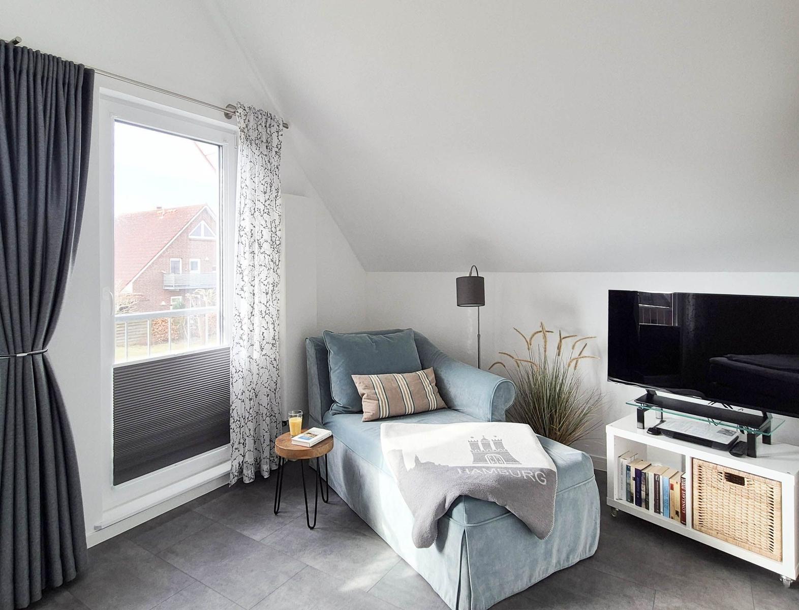 Ein Wohnzimmer mit Sofa, Fernseher und Fenster mit Blick auf eine Straße.