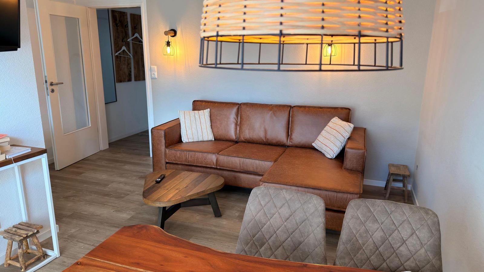 Wohnzimmer mit braunem Sofa, Holztisch und moderner Deckenleuchte.
