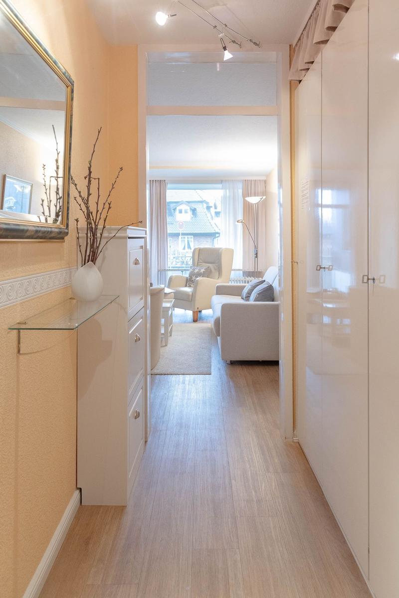 Flur mit Schrank und Spiegel führt in Wohnbereich mit Sofa und Sessel.