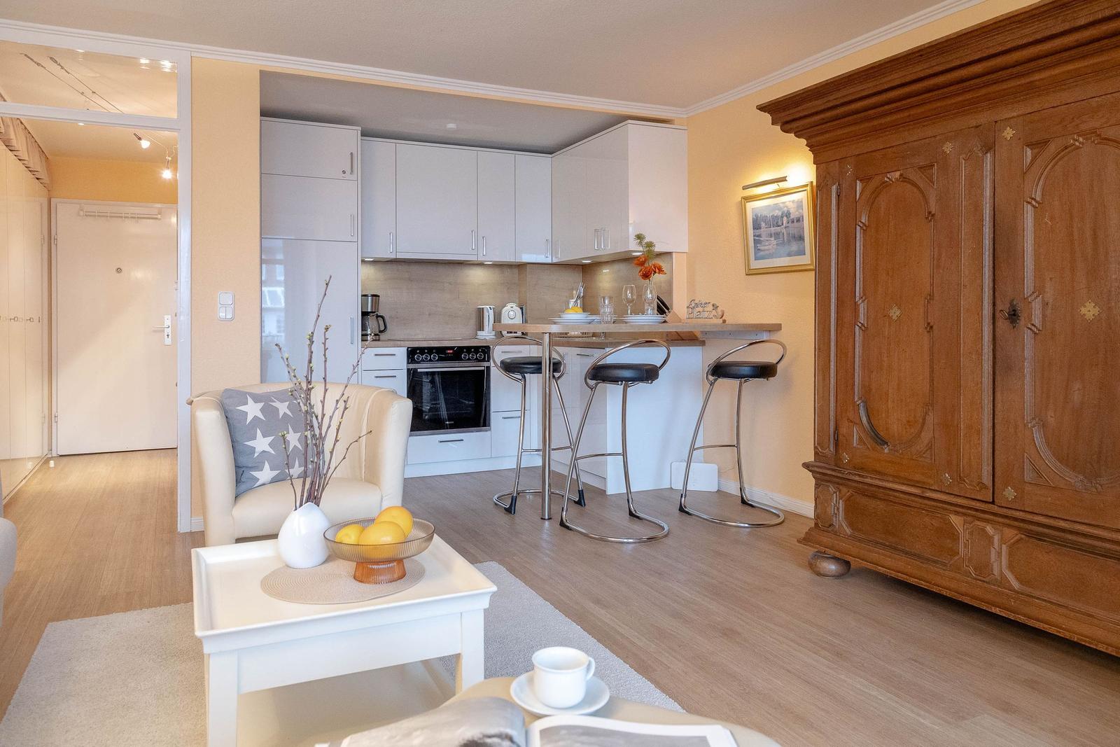 Wohnbereich mit Küchenzeile und Holzschrank. Esstisch mit Barhockern und Sessel.
