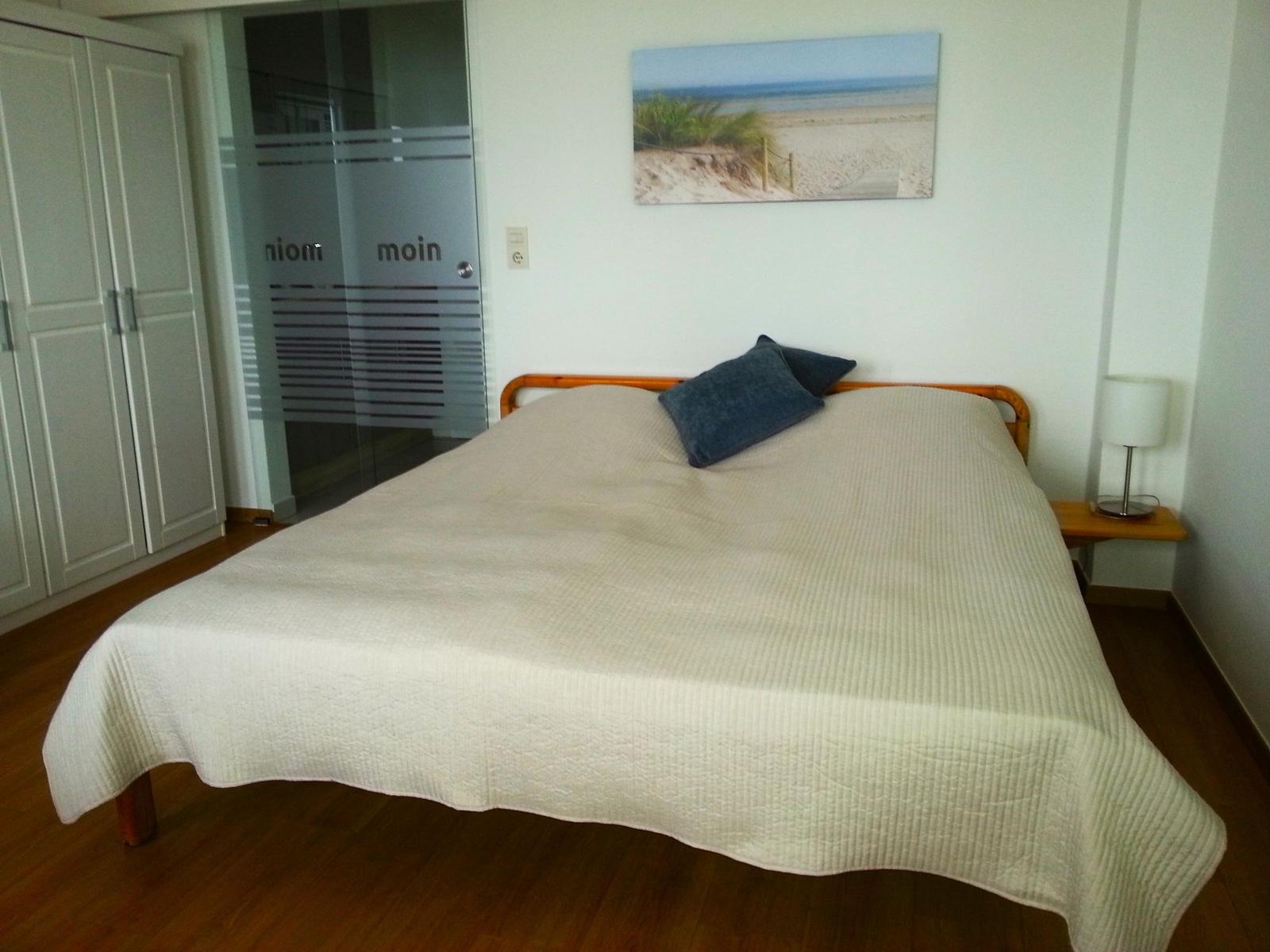 Schlafzimmer mit Bett, Kleiderschrank und Strandbild an der Wand.