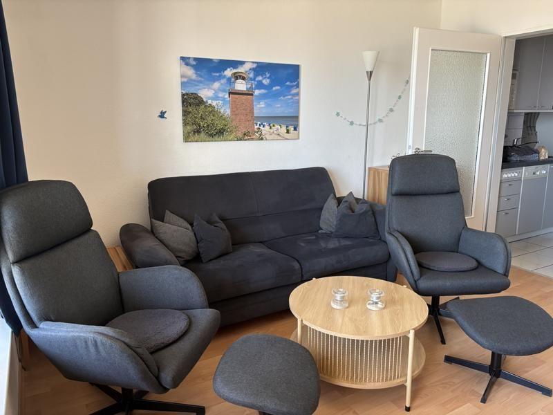 Living room with sofa, two chairs, and round table. Wall picture shows lighthouse.