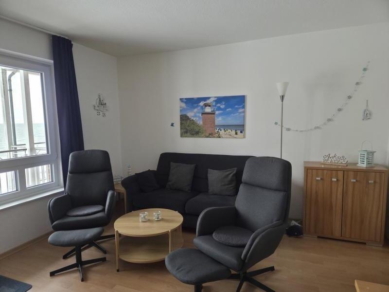 Living room with sofa, two chairs, table, and window with sea view.
