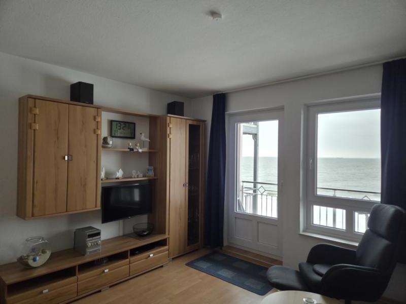 Living room with wooden furniture, TV, and sea view through windows and balcony door.