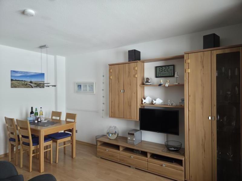 Living and dining area with wooden furniture, TV, and kitchenette.