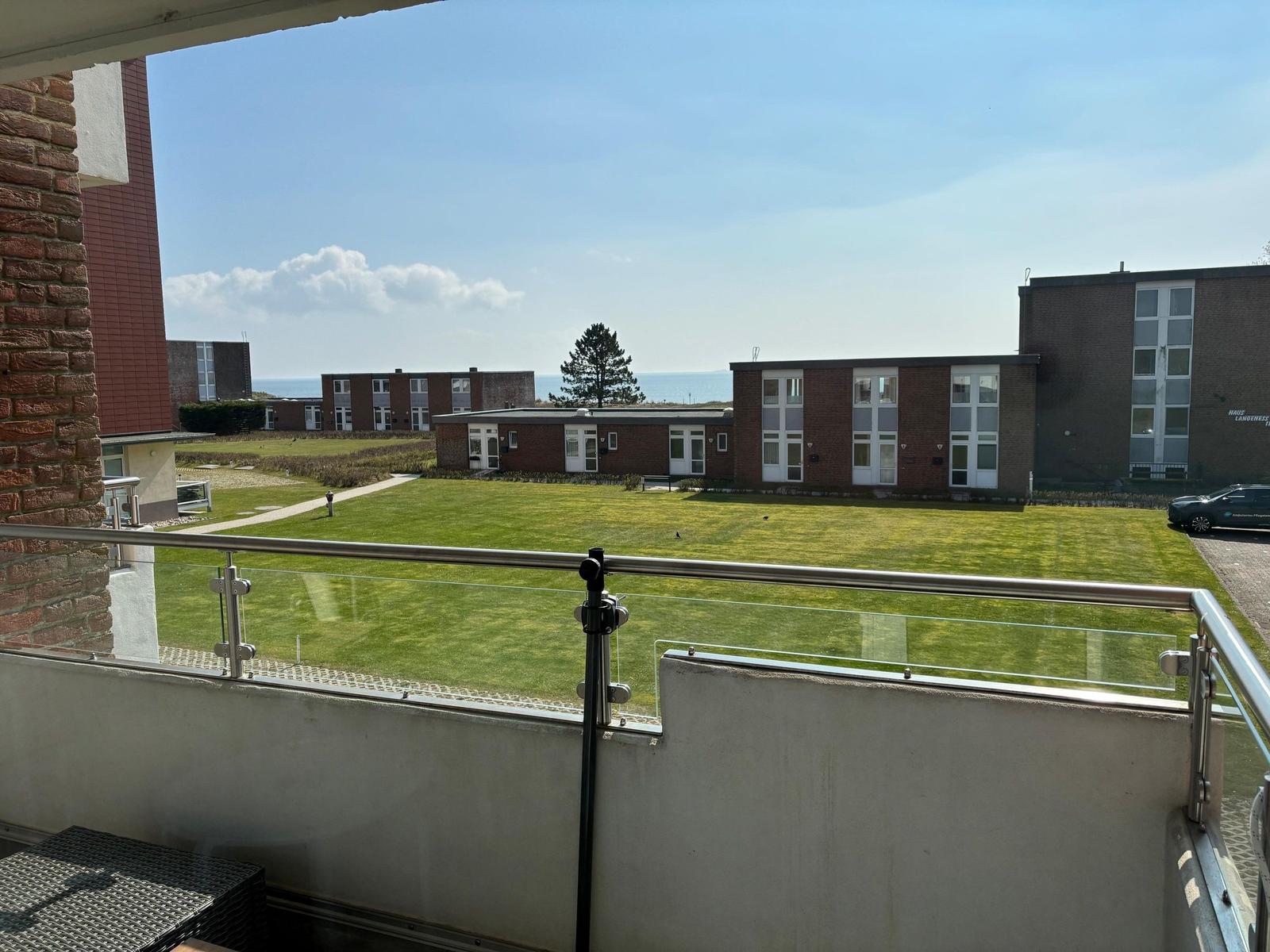 Terrasse mit Blick auf Grünfläche und Gebäude. Im Hintergrund ist das Meer sichtbar.