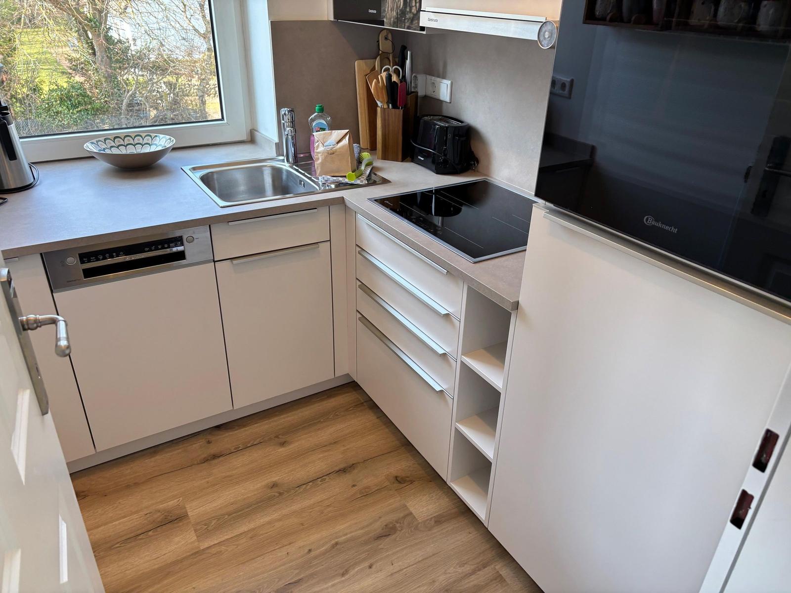 Küche mit Spüle, Herd und Kühlschrank. Holzboden und Fenster mit Blick nach draußen.