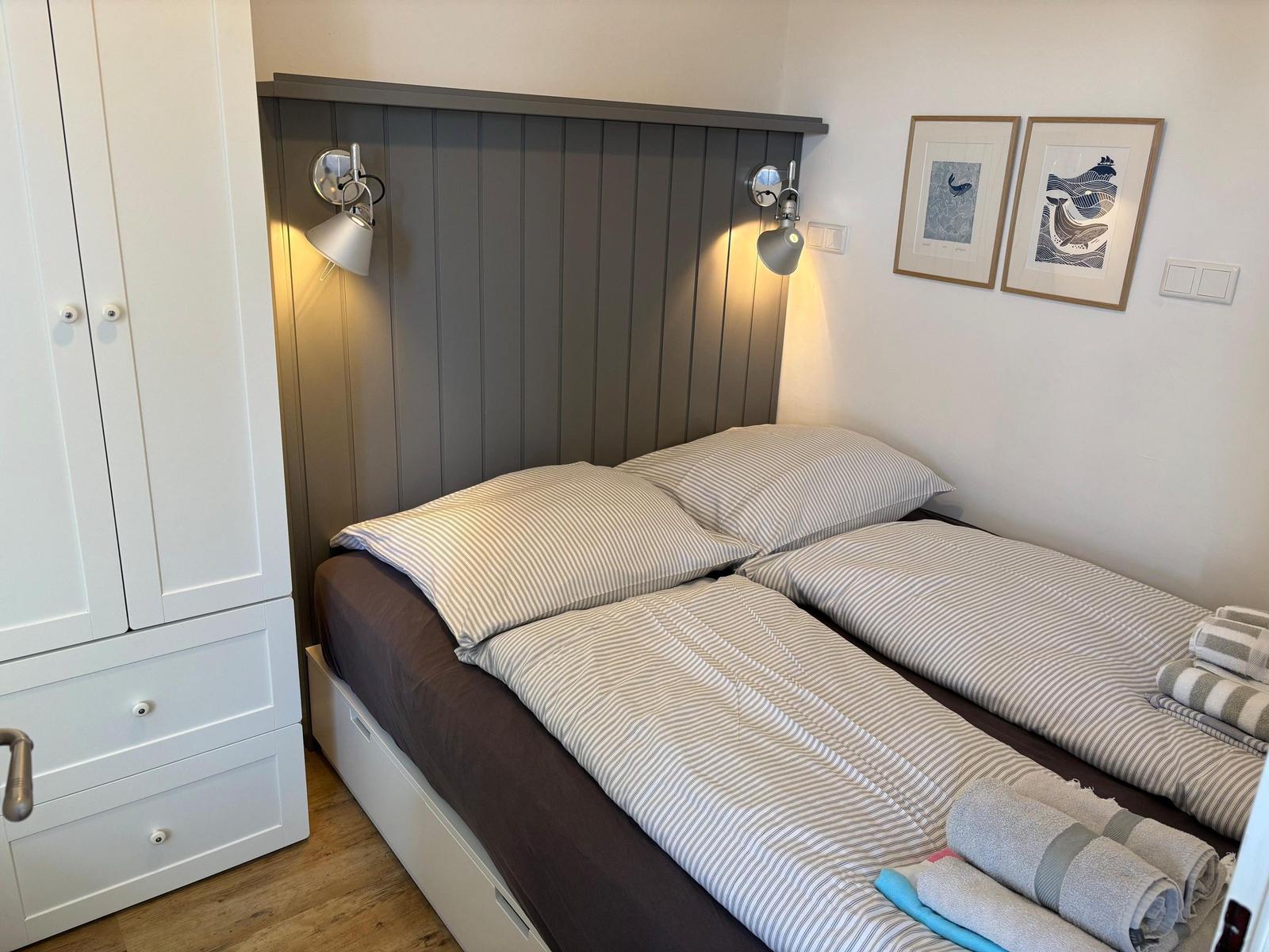 Schlafzimmer mit Doppelbett, grauem Kopfteil, weißen Schränken und gerahmten Bildern an der Wand.