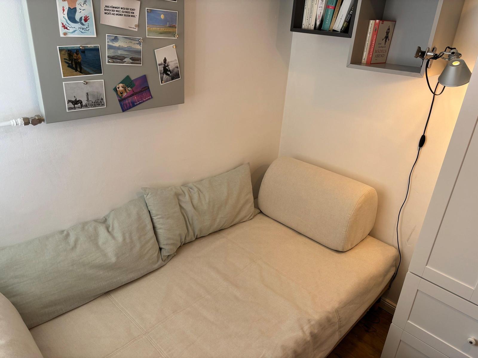 Ein Sofa mit Kissen und Wandregal mit Büchern und Bildern.