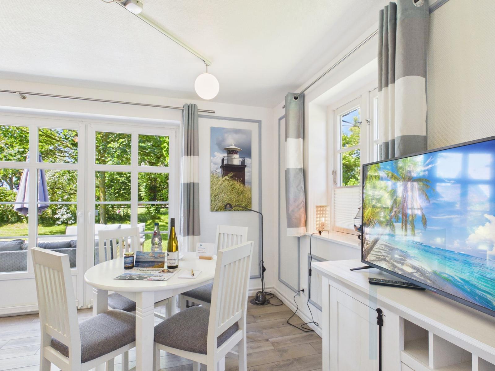Essbereich mit Tisch, Stühlen und TV. Fenster mit Blick auf Garten.