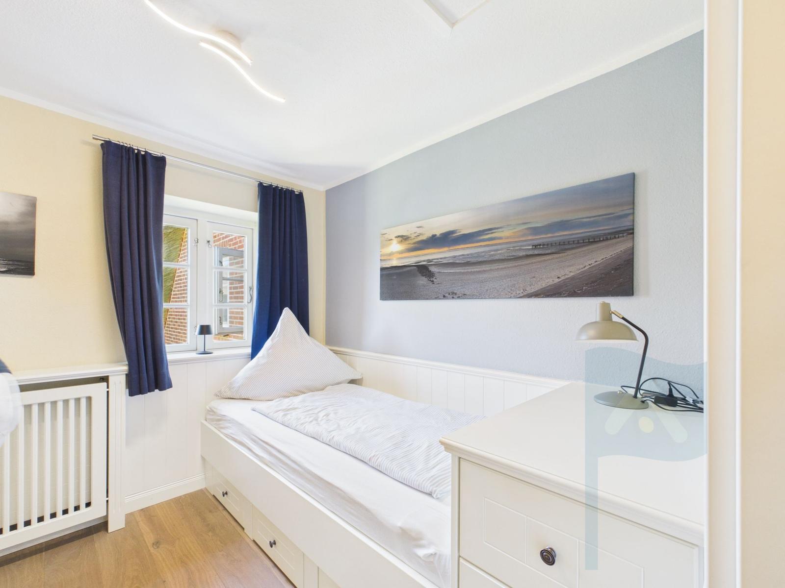 Schlafzimmer mit Bett, Schreibtisch und Wandbild. Fenster mit blauen Vorhängen.