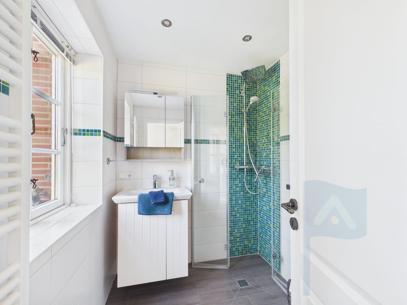 Badezimmer mit Dusche, Waschbecken und Fenster. Duschwand mit grünem Mosaik.