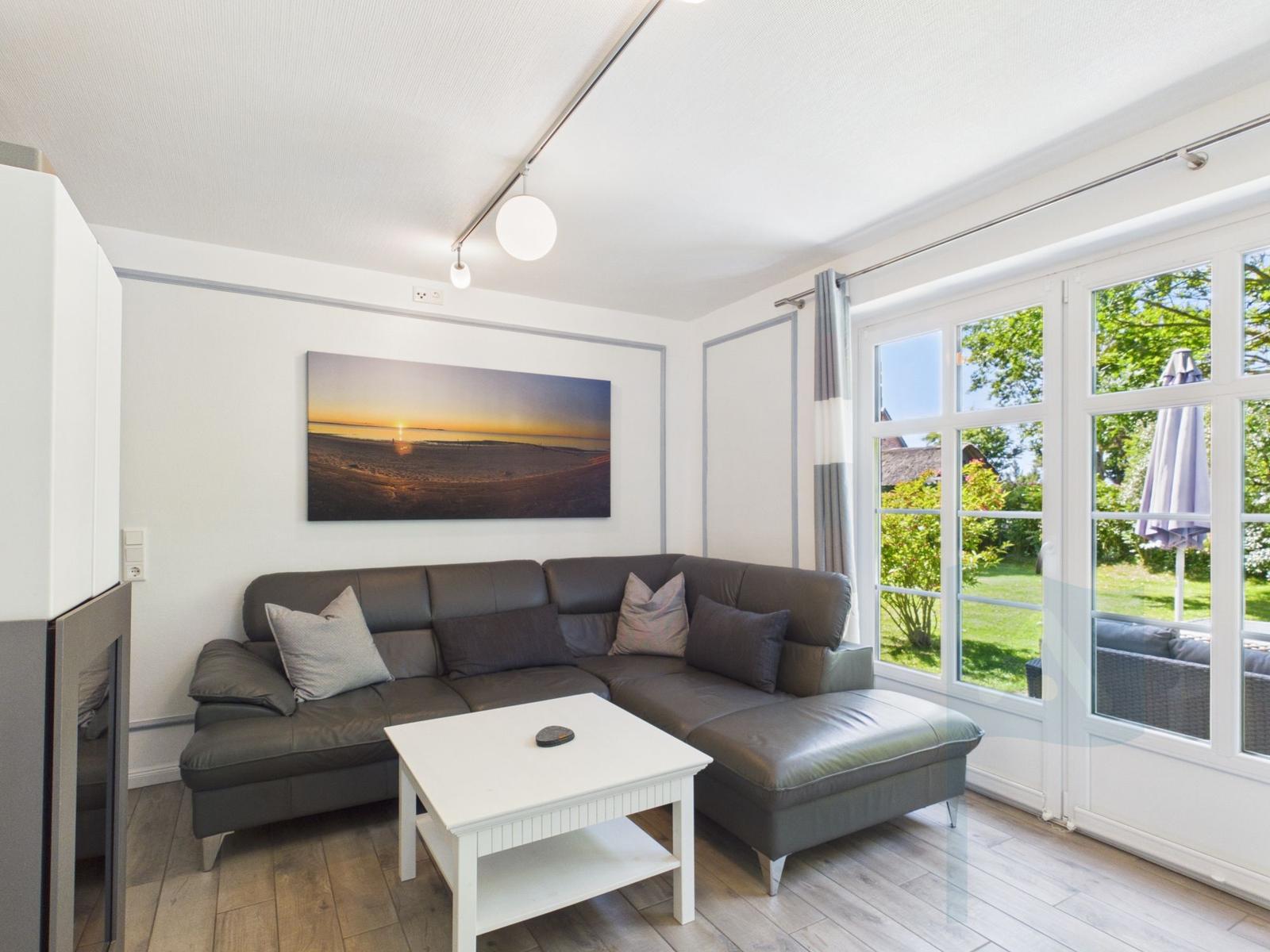 Wohnzimmer mit grauem Sofa, weißem Tisch und Fenster zur Terrasse.