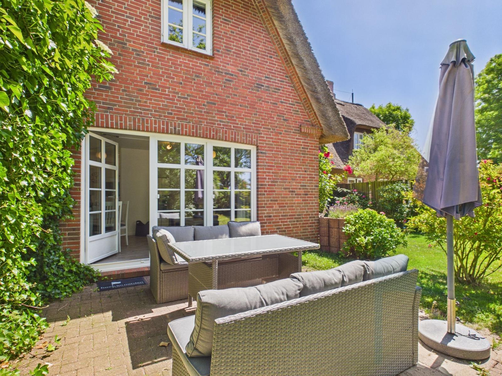 Roter Backsteinhaus mit Terrasse, Sitzgruppe und Sonnenschirm im Garten.