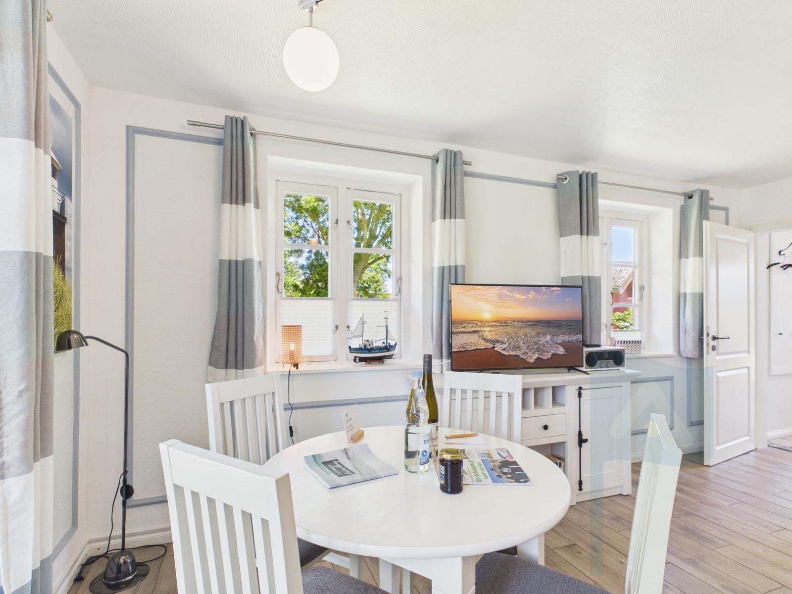 Wohn- und Essbereich mit TV, Tisch und Stühlen, Fenster mit Blick auf Bäume.