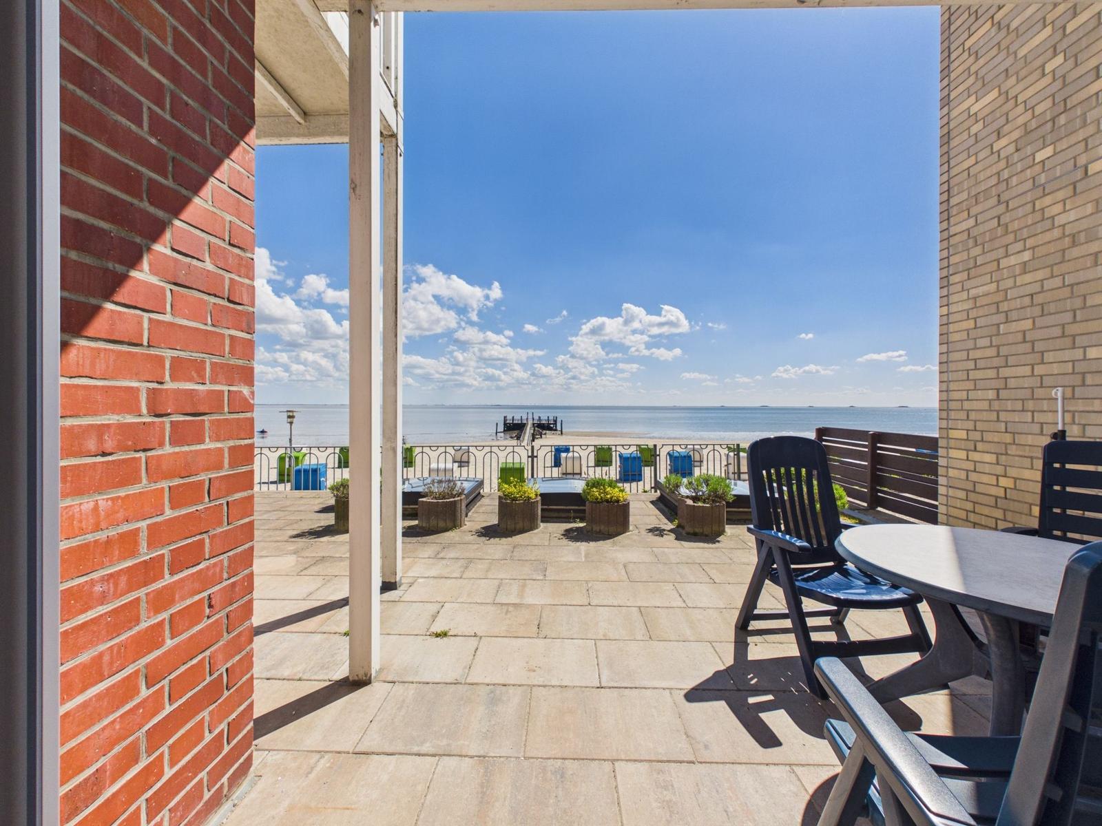 Terrace with table and chairs, view of beach and sea under blue sky.