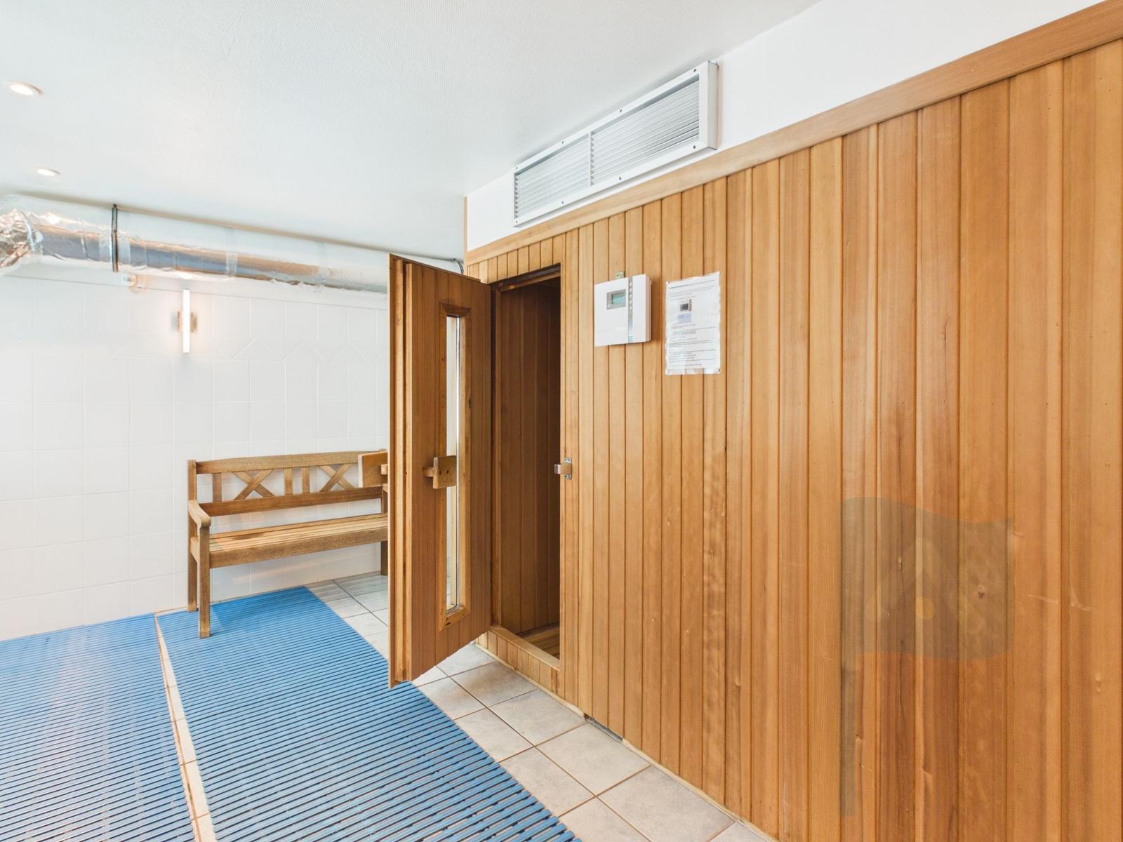 Sauna room with wooden wall and bench. Door open, floor with blue mat.