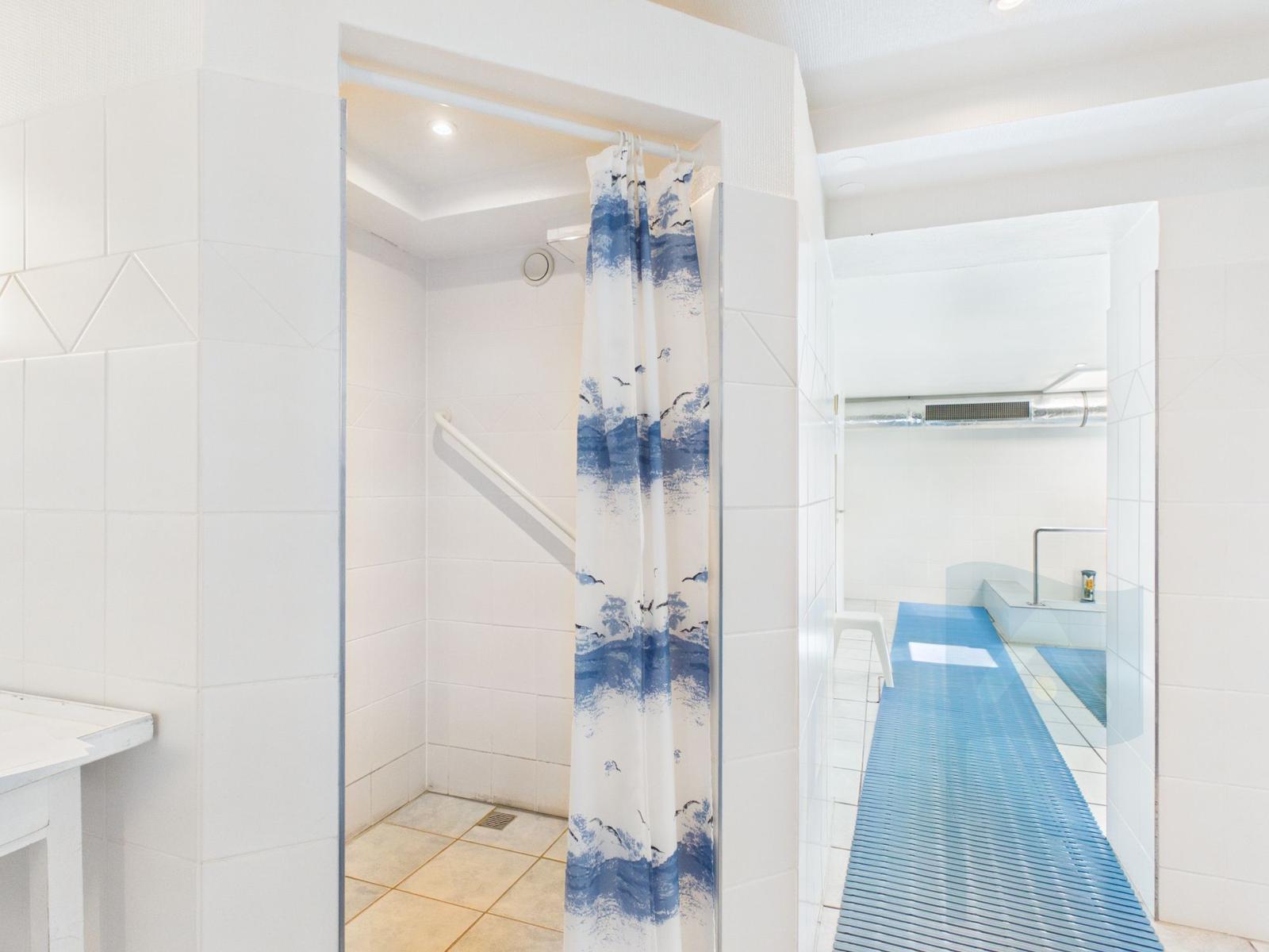 Shower with curtain, blue mat, and bathtub in the background.