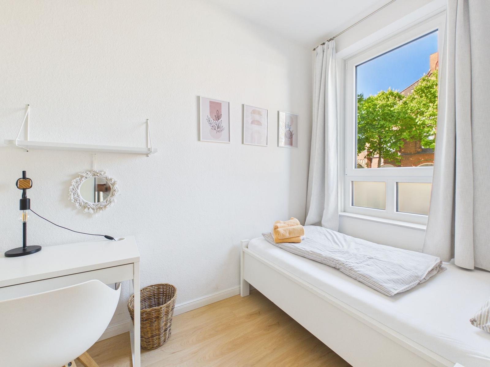 A bedroom with window, desk and bed. Three pictures hang on the wall.