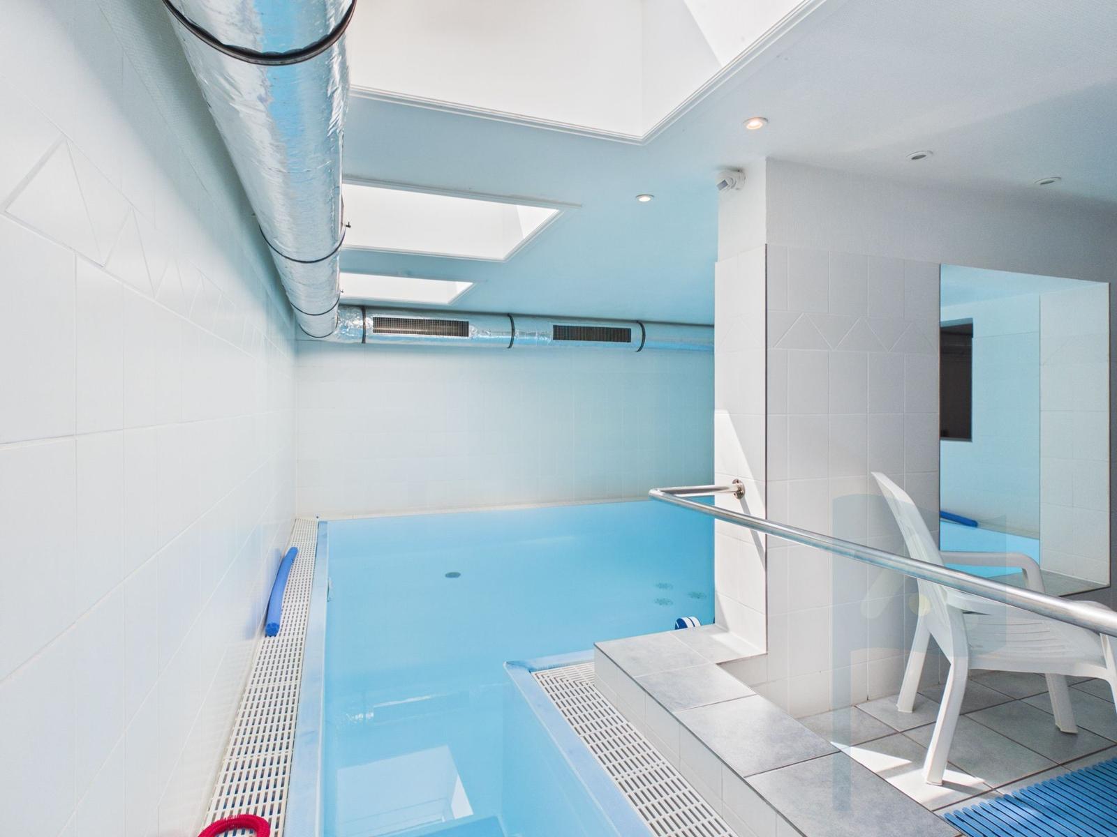 Indoor pool with white tiled walls and glass partition. Wooden steps and handrail.