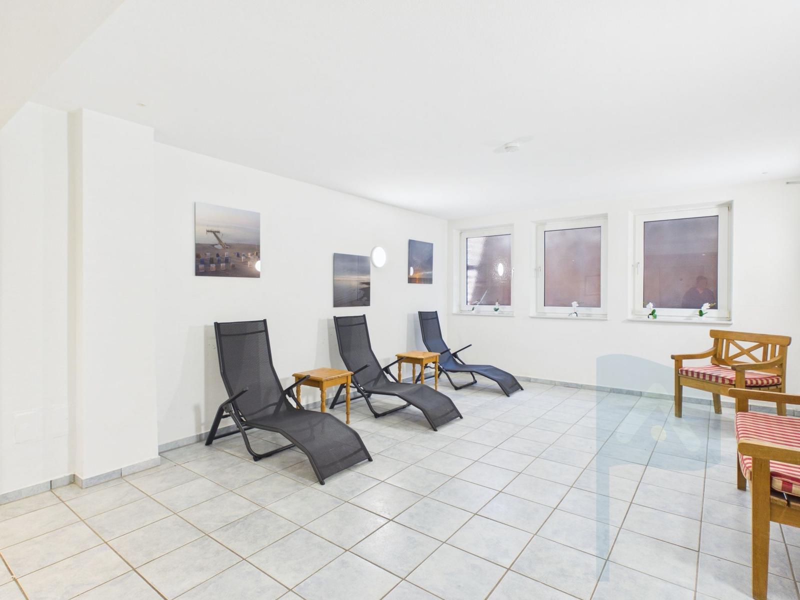 Room with lounge chairs, benches, and windows. Wall art and tiled floor.