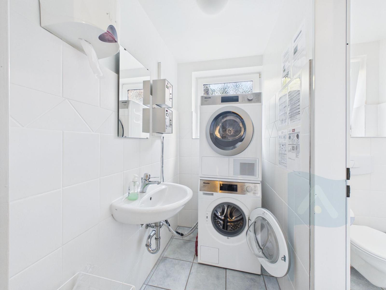 Washing room with washer and dryer, mirror, and towel dispenser.