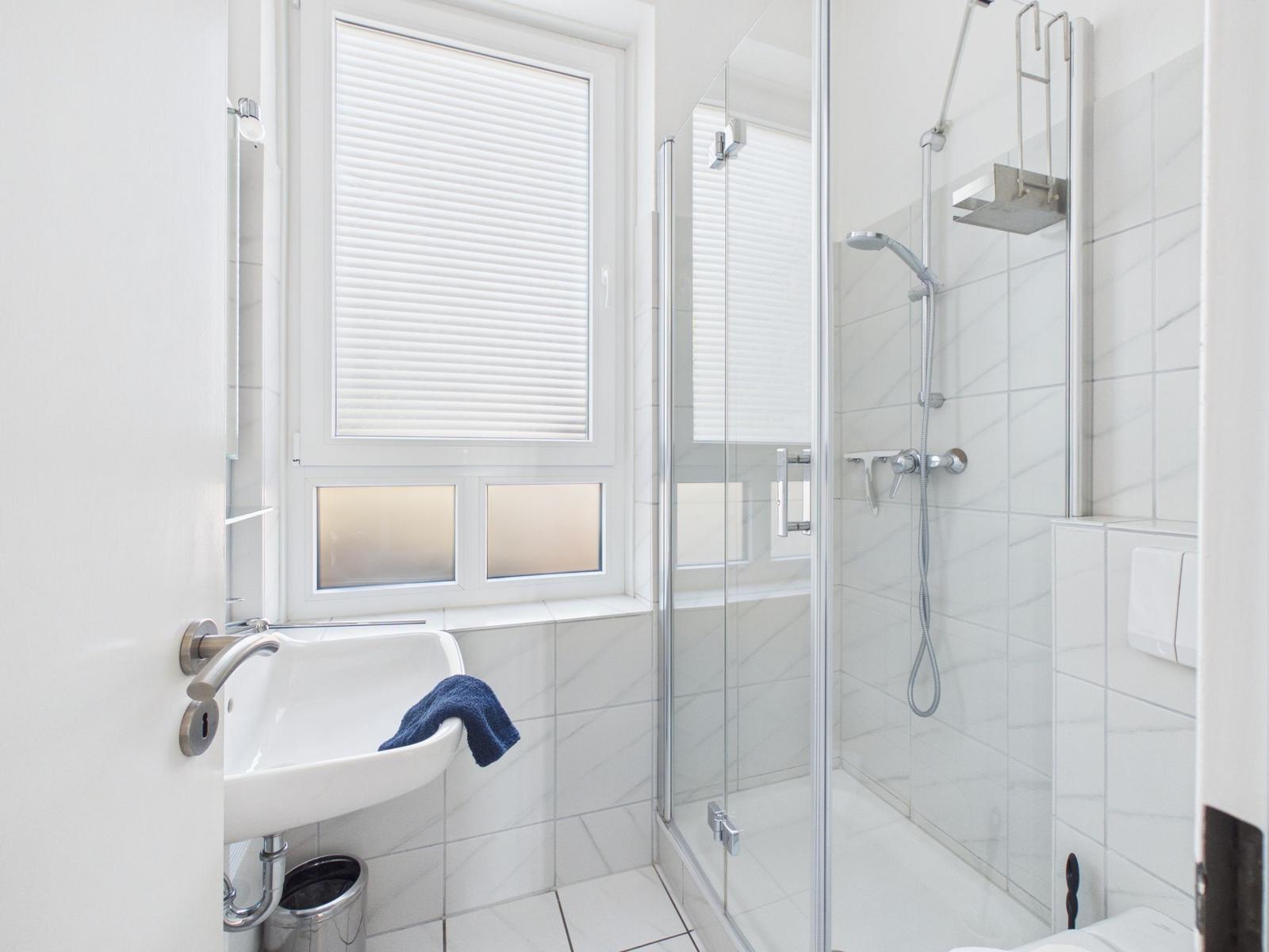 Bathroom with shower, sink, and window with blinds.