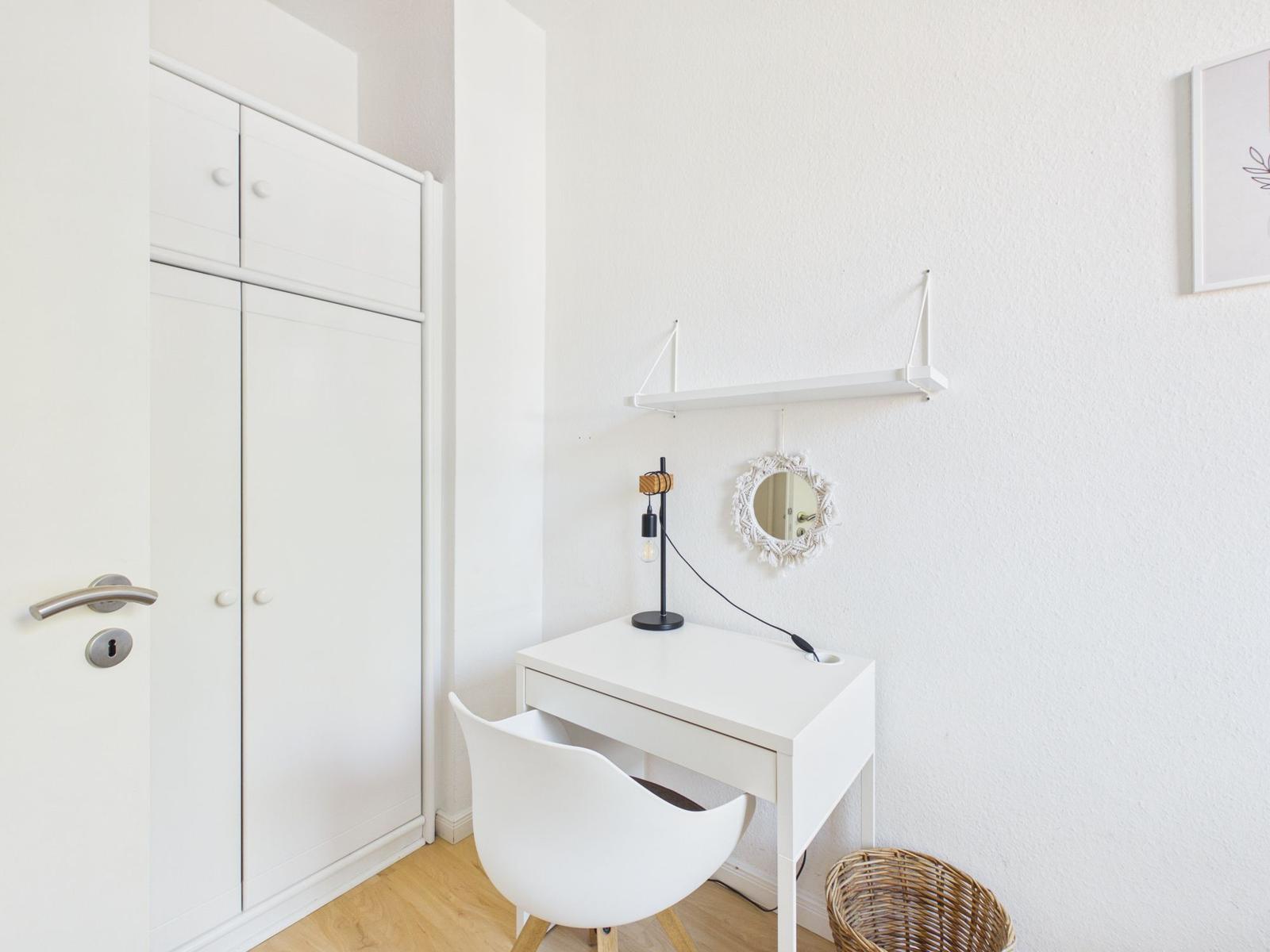 Desk with chair, mirror, and lamp in a room with wardrobe.