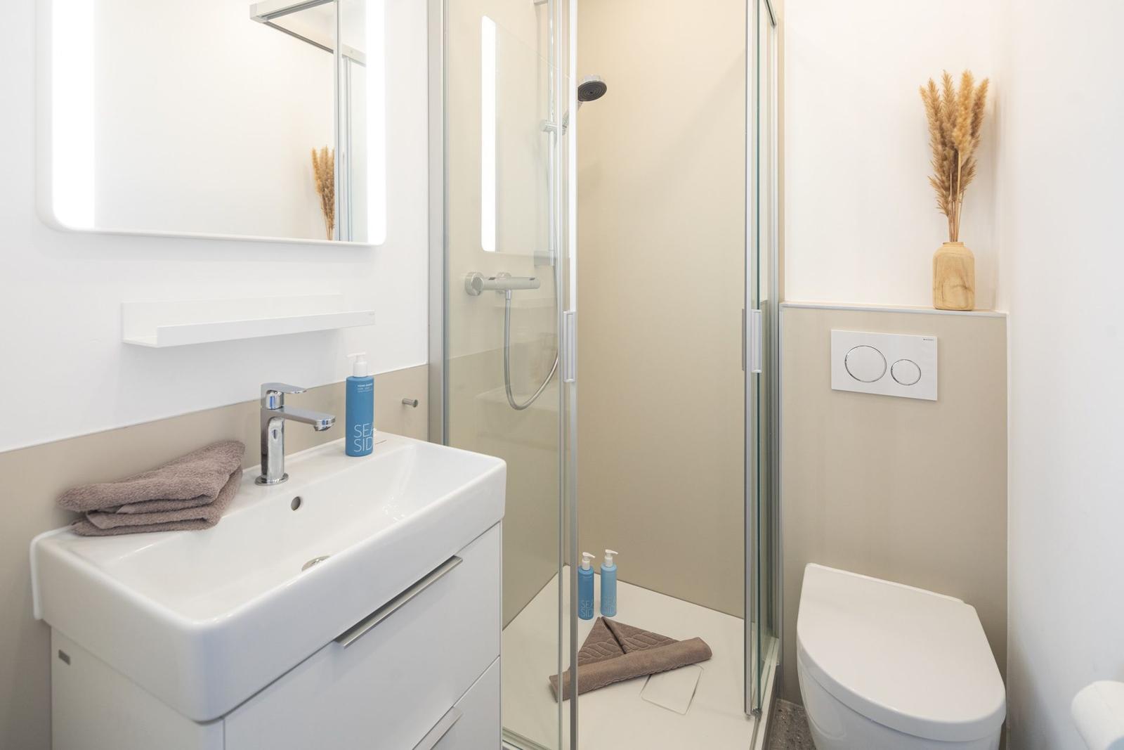Badezimmer mit Dusche, Waschbecken und Toilette. Moderne Einrichtung mit neutralen Farben.