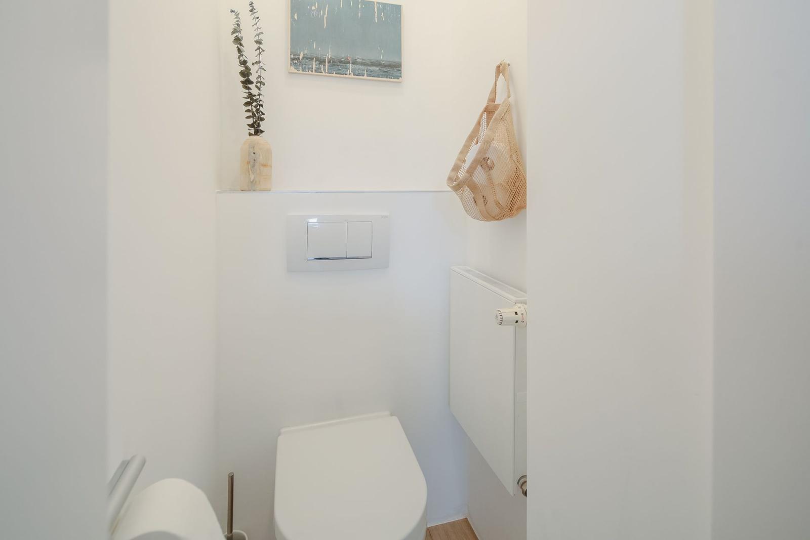 Toilet area with wall heater, decorative vase, and picture on the wall.