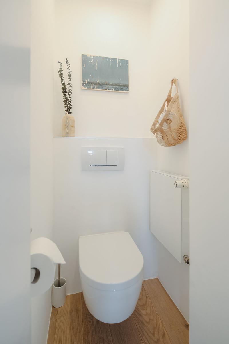 Toilet with wooden floor, wall heater, and decorative wall decor.