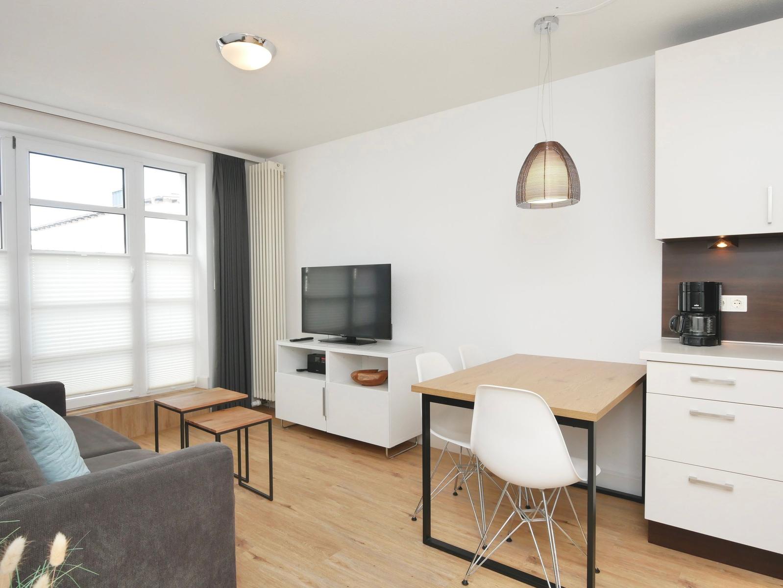 Wohnbereich mit Sofa, Esstisch, TV und Küchenzeile.