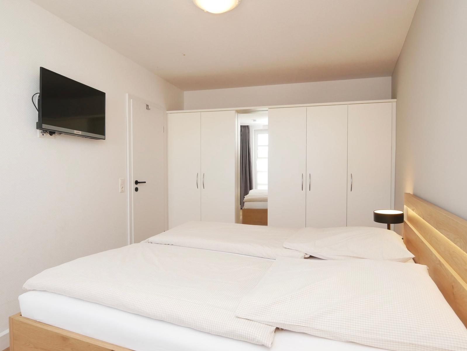 Schlafzimmer mit Doppelbett, weißen Schränken und Wandfernseher.