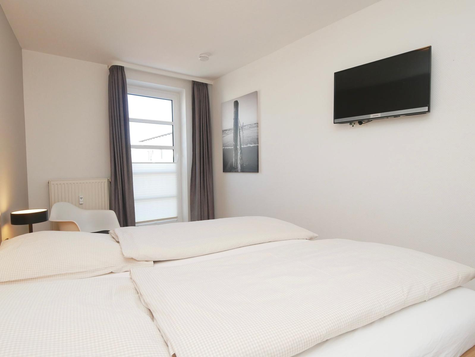 Schlafzimmer mit Doppelbett, Wandbild, Fenster und Wandfernseher.