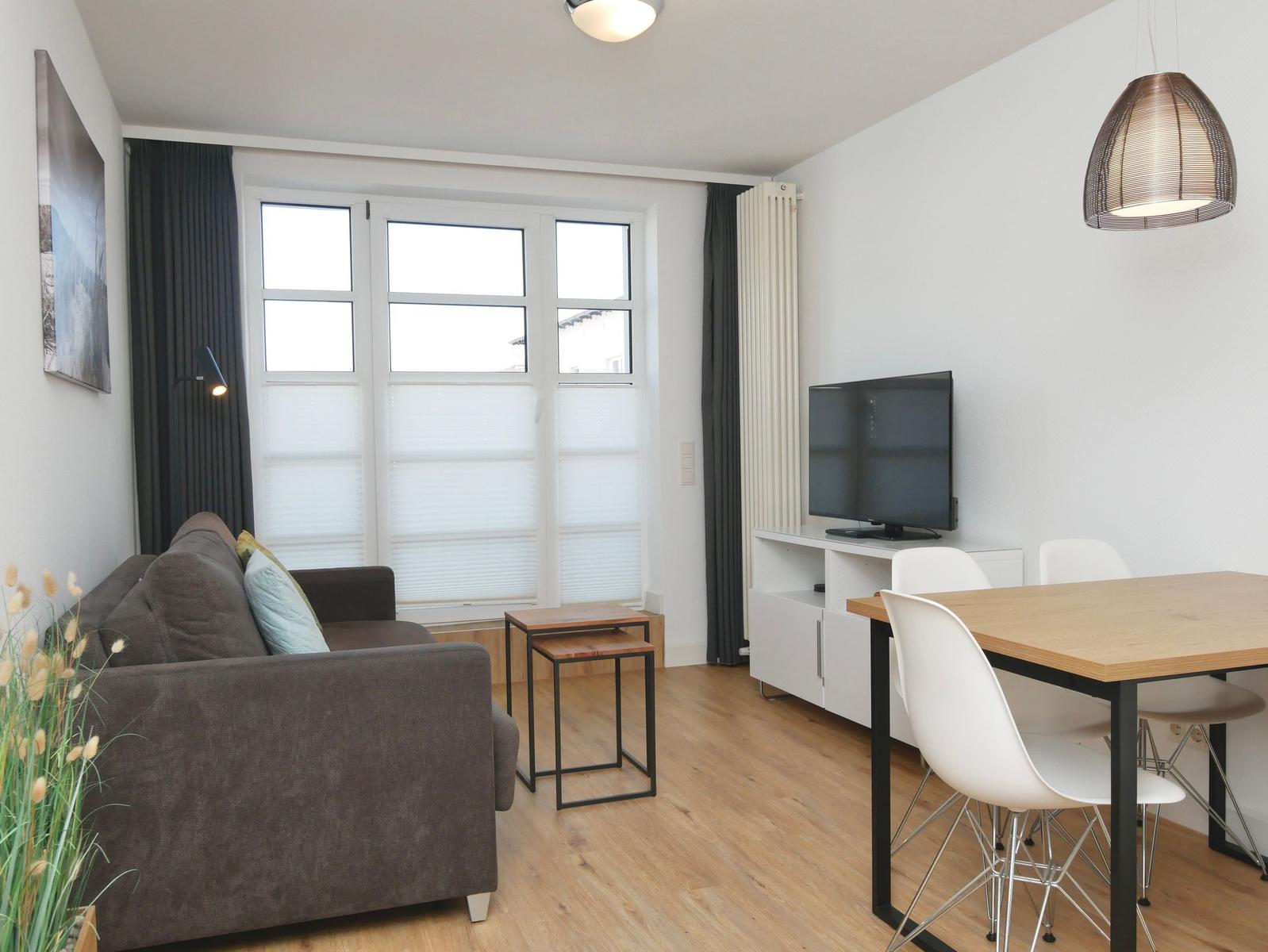 Wohn- und Essbereich mit Sofa, TV und Esstisch mit Stühlen.