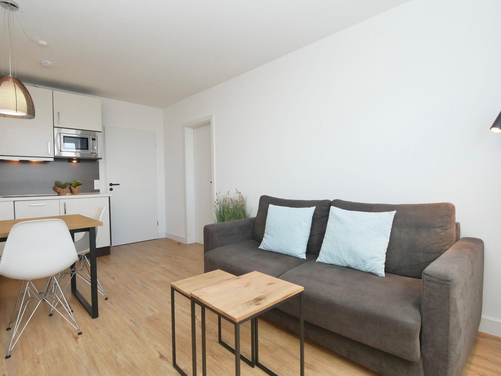 Wohnbereich mit Sofa, Tisch und Küchenzeile im Hintergrund.