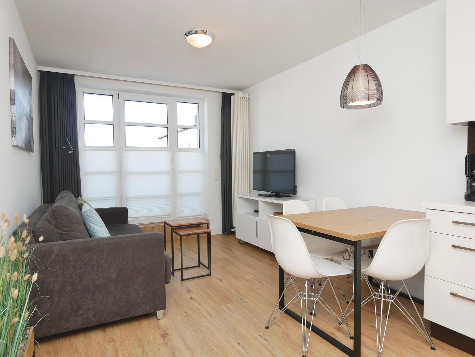 Wohn- und Essbereich mit Sofa, Esstisch, Fernseher und Holzboden.