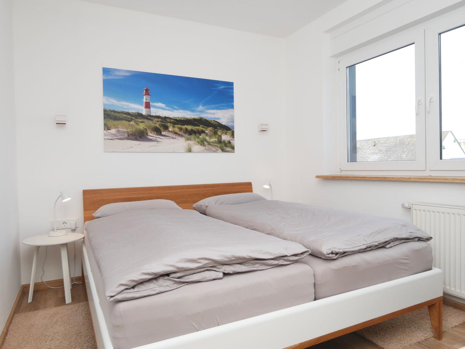Schlafzimmer mit Doppelbett, Wandbild und Fenster.
