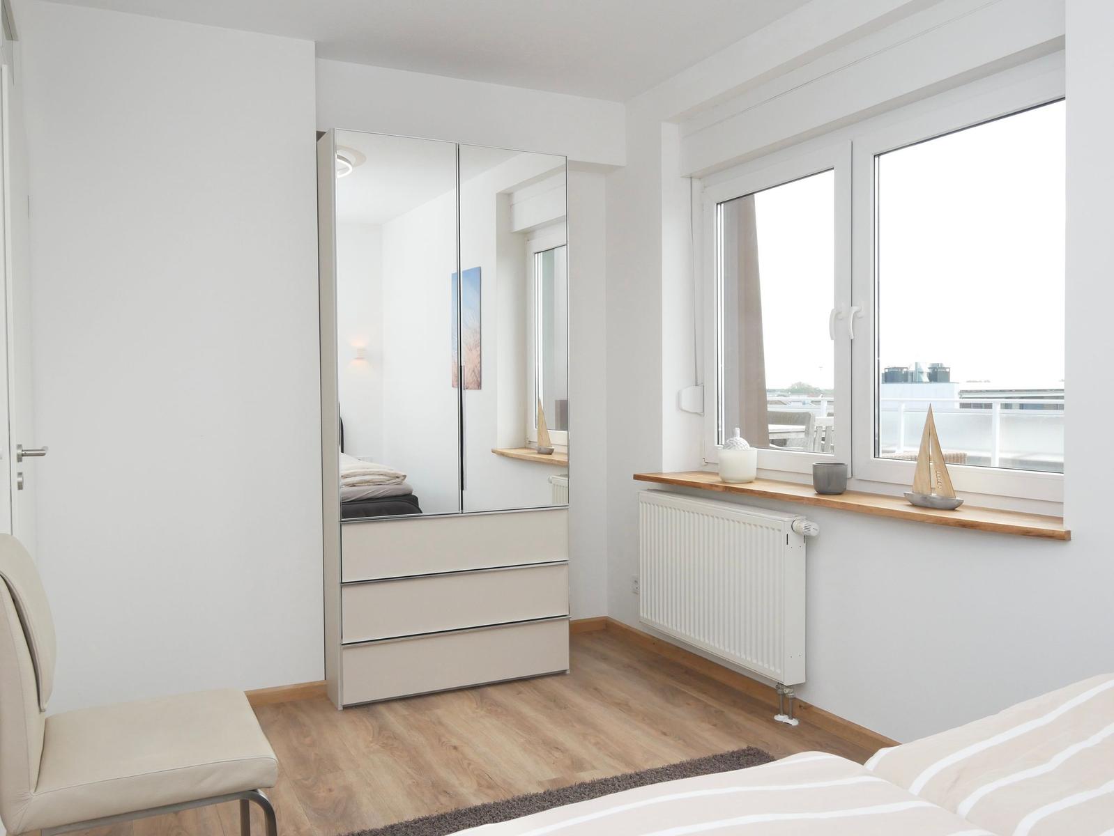 Schlafzimmer mit Spiegelschrank, Fenster und Holzboden.