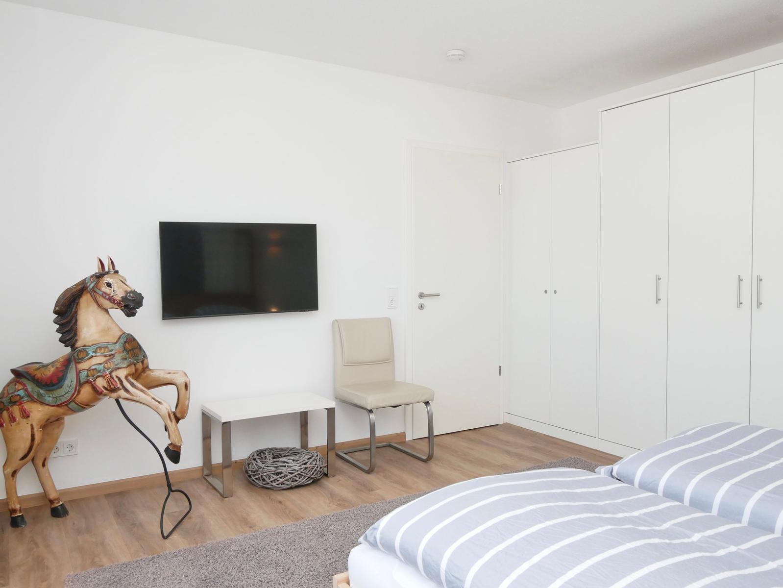 Schlafzimmer mit Bett, Kleiderschrank, TV und Pferdstatue.